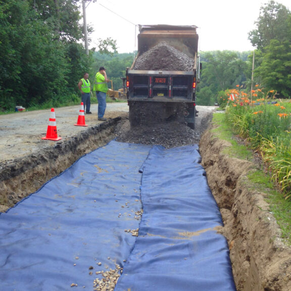 Installing Mirafi H2Ri along a roadside for high-strength ground reinforcement.