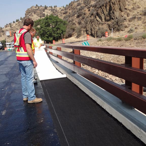 Contractors simply peeling off the back of Petrotac Self-Adhesive Paving Membrane & installing it on a bridge