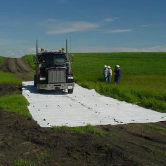 Heavy equipment driving on mud mats across a green field without damaging the grass