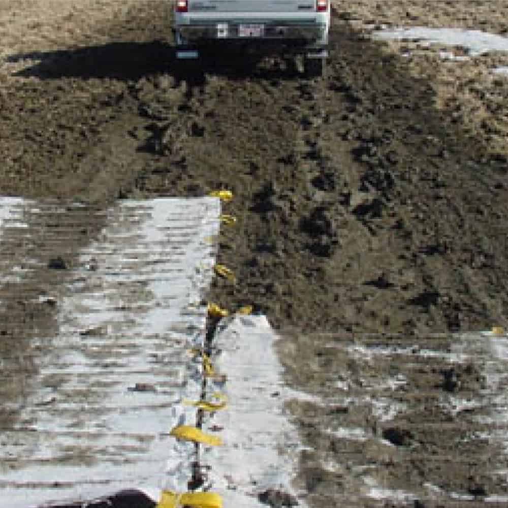 Construction trucks driving across a muddy and rutted access road without getting stuck due to the mud mats that are laid down