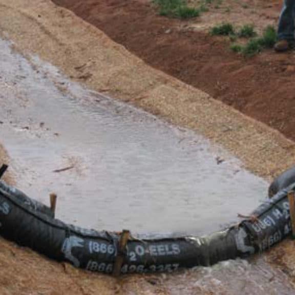 A silt fence placed on top of gravel and soil and laid across a small waterway