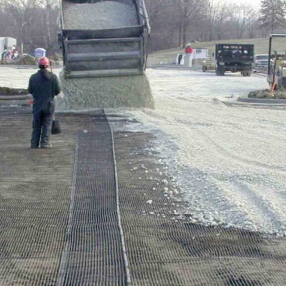 Construction professionals installing aggregate over biaxial geogrid for increased ground support and base stabilization