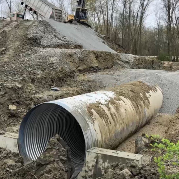 Construction professionals burying corrugated metal drainage pipe with stone and sand