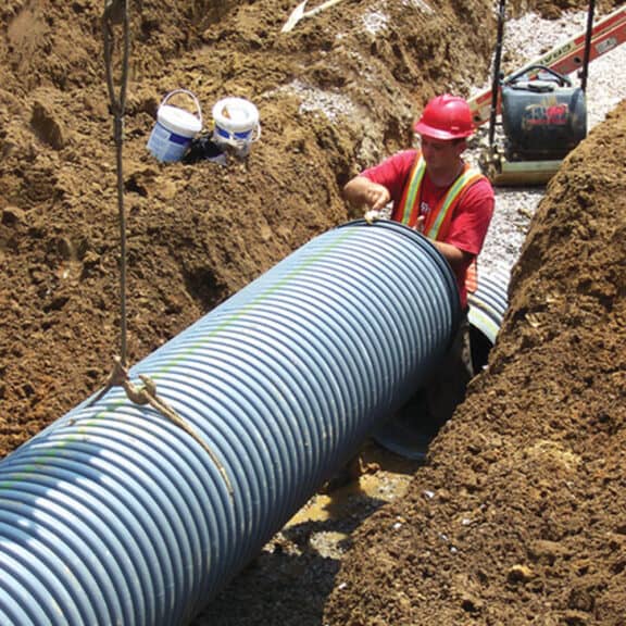 A professional installing corrugated HDPE pipe underground