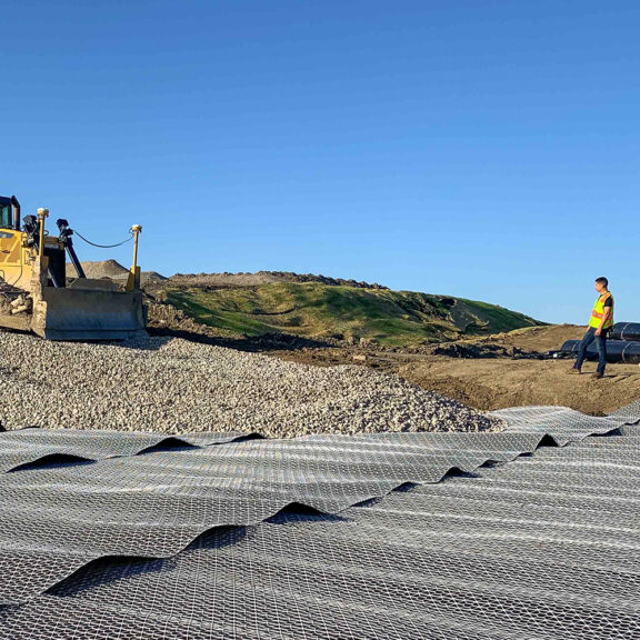 Construction professionals adding aggregate on top of Tensar FilterGrid across a sloping landscape