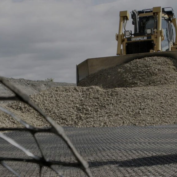 Large bulldozer covering triaxial geogrid with aggregate while building a roadway